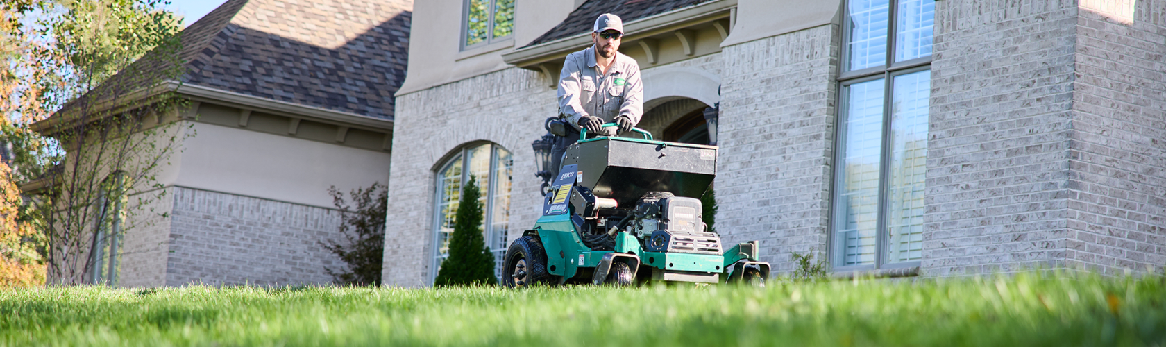 man on aeration and seeding machine with house in background